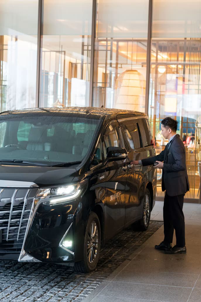 A chauffeur opens the door of a black people mover at a hotel entrance