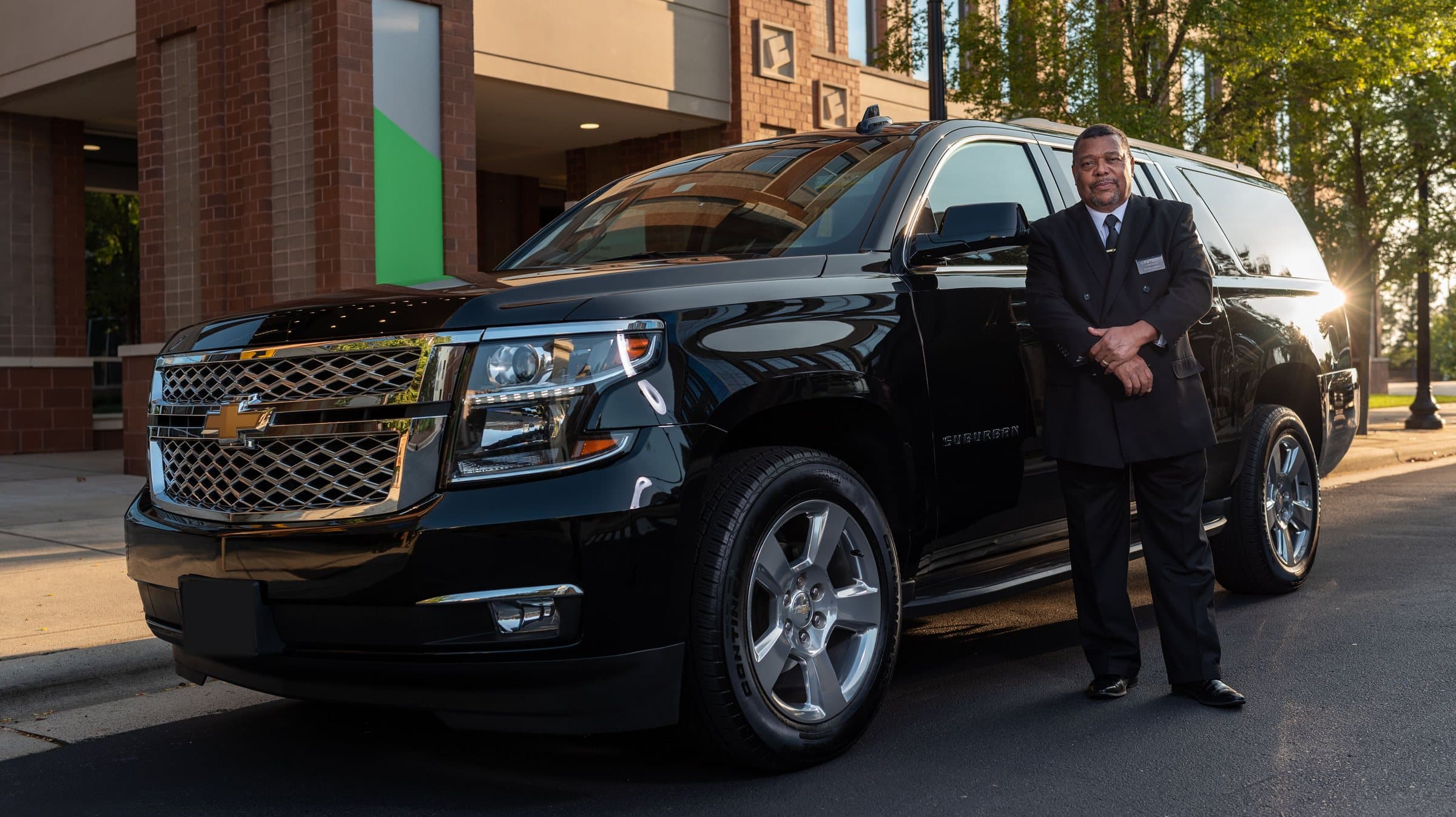 A large black SUV with a chauffeur standing beside it