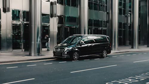 A black luxury people mover parked beside a glass-fronted building